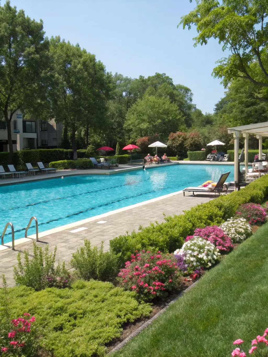 A luxurious outdoor swimming pool with comfortable lounge chairs and umbrellas, surrounded by lush greenery, illustrating relaxation and leisure at ApexResidences.